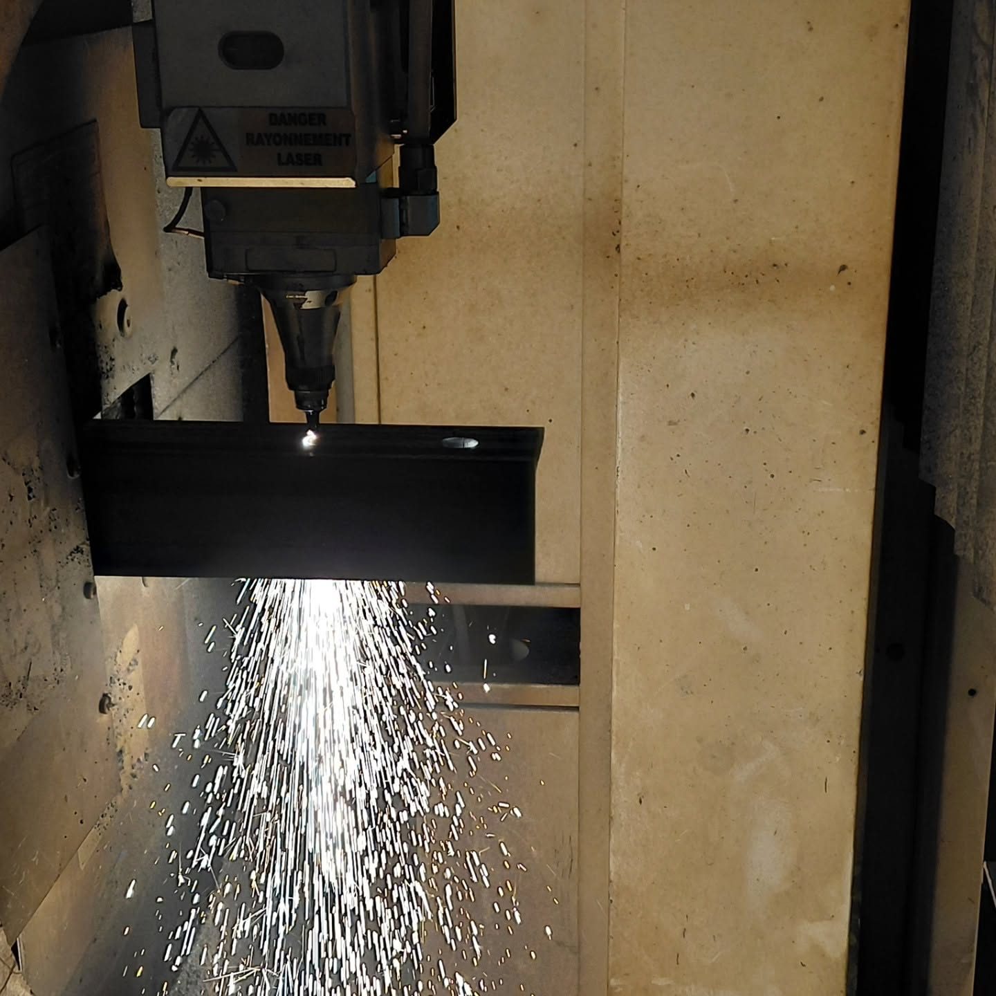 Tête de découpe laser en action sur un profilé acier, gerbe d'étincelles — atelier Fer'Play