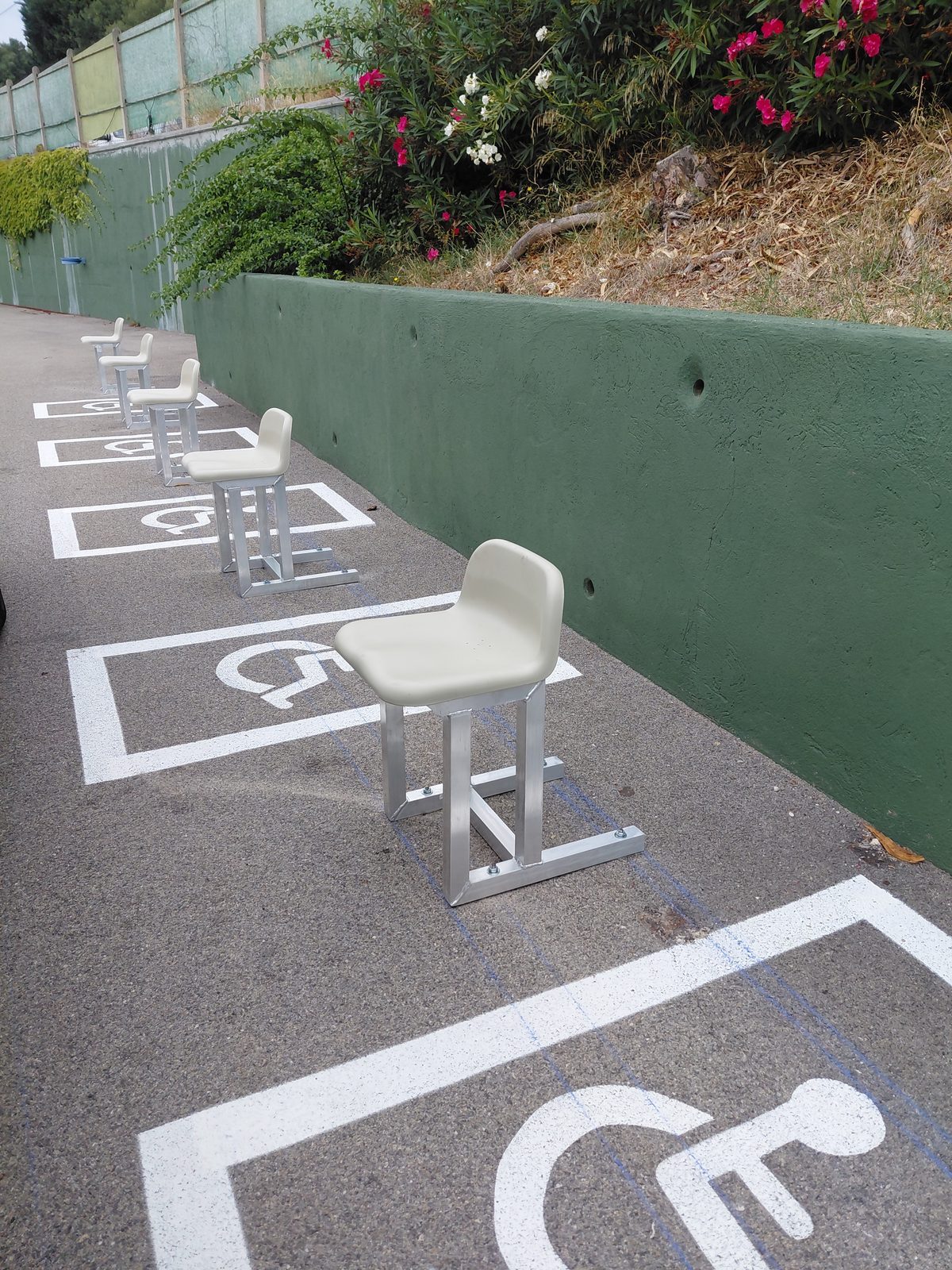 Sièges d'accompagnant PMR à structure aluminium et assise plastique, alignés sur les emplacements fauteuil roulant — stade du Pignier, Cassis